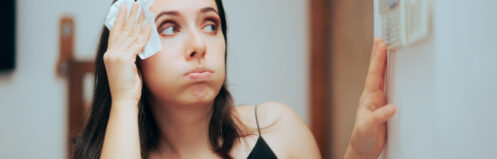 Woman blotting sweat from her forehead while adjusting the thermostat