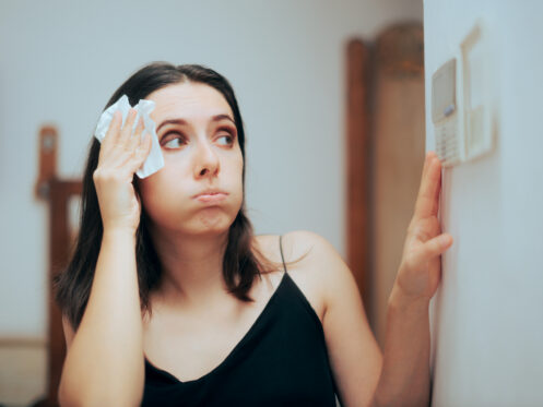 Woman blotting sweat from her forehead while adjusting the thermostat